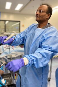 A surgeon at work, wearing blue scrubs and gloves.